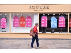 WORCESTER-ENGLAND - MARCH 27: A lady wearing a mask walks past a closed Joules shop in Worcester Town Center on March 27, 2021 in Worcester, England .