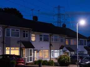 An electricity transmission tower near residential houses with lights on in Upminster, UK, on ​​Monday, July 4, 2022. The UK is set to water down one of its key climate change policies as it battles soaring energy prices that have contributed to a cost- of-living crisis for millions of consumers. Photographer: Chris Ratcliffe/Bloomberg