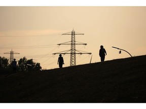 High voltage electricity towers beyond pedestrians on a river bank in Hamburg, Germany, on Wednesday, Aug. 24, 2022. German power surged to above 700 euros ($696) a megawatt-hour for the first time as panic over Russian supplies gripped markets and politicians warned citizens to brace for a tough winter ahead.