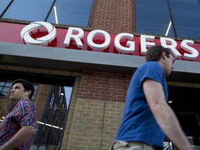 Pedestrians pass in front of a Rogers Communications Inc. store in Toronto.