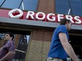 Pedestrians pass in front of a Rogers Communications Inc. store in Toronto.