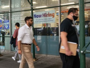 A 'now hiring' sign is displayed in a window in Manhattan, New York City.