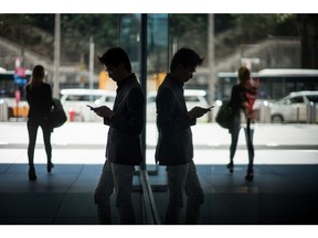 A man is reflected in a window while using a smart phone in Hong Kong, China, on Wednesday, Nov. 22, 2017. Hong Kong's benchmark equity gauge rose above the 30,000 level for the first time in a decade as Tencent Holdings Ltd. extended its rally and Chinese financial shares climbed. Photographer: David Paul Morris/Bloomberg