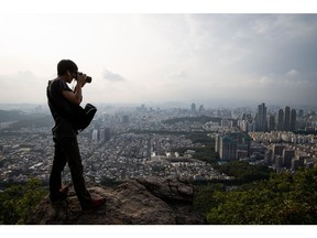 A man takes a photograph of the city skyline from the Guryong Mountain in Seoul, South Korea, on Friday, July 12, 2019. Investors await the nation's GDP report on July 25 after the central bank said it was ready to consider further policy response if growth worsens. Photographer: SeongJoon Cho/Bloomberg