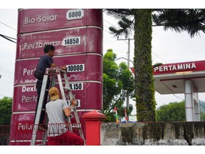 Workers change fuel prices on a gas station board in Pangkal Pinang on Sept. 5.