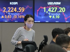 A currency trader passes by screens showing the Korea Composite Stock Price Index (KOSPI), left, and the exchange rate of South Korean won against the U.S. dollar at the foreign exchange dealing room of the KEB Hana Bank headquarters in Seoul, South Korea, Tuesday, Sept. 27, 2022.