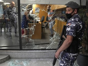 FILE - A Lebanese policeman stands guard next to a bank window that was broken by depositors to exit the bank after attacking it trying to get blocked money, in Beirut, Lebanon, Wednesday, Sept. 14, 2022. A Lebanese activist group said they will continue to organize bank raids to help people retrieve their trapped savings. Activists from the Depositors' Outcry group made these remarks at a press conference on Thursday, after activists helped Sali Hafez retrieve $13,000 in her savings to help fund her sister's cancer treatment on Wednesday.