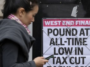 A woman walks past a headline posted on a wall in London. The Bank of England and the British government try to soothe markets nervous about a volatile U.K. economy and currency.