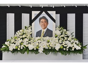 An image of former Japanese prime minister Shinzo Abe is displayed at the stands set up outside the Nippon Budokan in Tokyo on September 27, 2022, as people queue up to leave flowers and sign a condolence book ahead of his state funeral.  Photographer: Yuichi Yamazaki/AFP/Getty Images