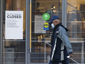 A man wearing a face mask walks past a closed clothing store in Toronto.