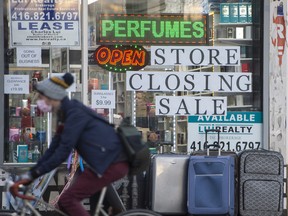 A cyclist wearing a mask rides past a 'Store Closing Sale' sign while travelling north on Toronto’s Spadina Avenue.