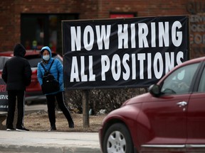 People standing near a sign indicating that a local business is hiring in Winnipeg.