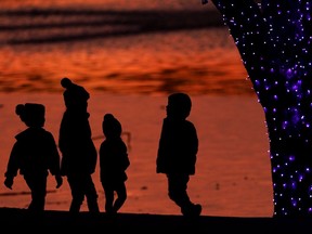 FILE - In this Dec. 26, 2020 file photo, children are silhouetted against a pond as they look at Christmas lights at a park in Lenexa, Kan. Custodial accounts are a way to invest for minors and give them a headstart on building wealth. How can you ensure they're financially responsible enough to manage their assets when they reach the age of majority? One way is to share your money values with them and teach budgeting basics as well as saving tactics early on.