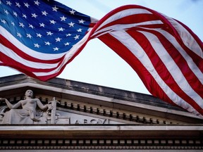 FILE - An American flag flies outside the Department of Justice in Washington, March 22, 2019. The Justice Department says three Iranian citizens have been charged in the United States with cyberattacks that targeted power companies, local governments and small businesses and nonprofits, including a domestic violence shelter.