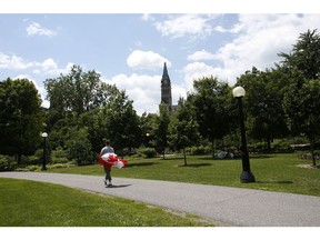 A pedestrian carrying a Canadian flag walks through a nearly empty Majors Hill Park on Canada Day in Ottawa, Ontario, Canada, on Wednesday, July 1, 2020. The Covid-19 pandemic has led to the cancellation of events on Parliament Hill in favor of online offerings to keep crowds from gathering, Canadian Press reported.