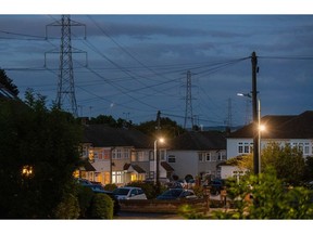 Electricity transmission towers near residential houses with lights on in Upminster, UK, on Monday, July 4, 2022. The UK is set to water down one of its key climate change policies as it battles soaring energy prices that have contributed to a cost-of-living crisis for millions of consumers.