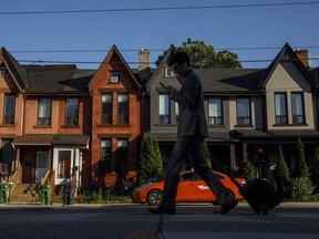 A person walks by a row of houses in Toronto on Tuesday July 12, 2022. TD Economics has revised its housing forecast to account for even steeper price declines in early 2023 and then slower growth for the remainder of the year.THE CANADIAN PRESS/Cole Burston