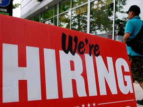 A man walks past a 'we're hiring' sign posted outside of a restaurant.
