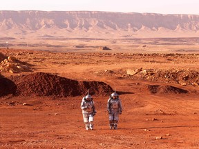 A couple of astronauts walk in spacesuits during a training mission for planet Mars.