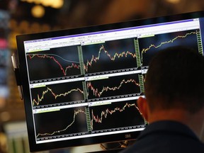 A screen displays stock charts while a trader works at his post on the floor at the New York Stock Exchange.