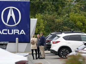 FILE - A salesman talks with customers in an Acura dealership lot in Wexford, Pa., on Sept. 29, 2022. New vehicle sales in the U.S. are expected to have fallen slightly in the third quarter, even with improvement in September. But there are warning signs that consumers' appetite for expensive new cars, trucks and SUVs may be waning.