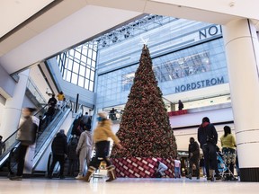 People pass a large Christmas tree as they go shopping on Christmas Eve at a mall in Ottawa on Dec. 24, 2020. A new report from Deloitte Canada says holiday spending in Canada is expected to drop this year as inflation shrinks consumer buying power and economic uncertainty looms over household finances.