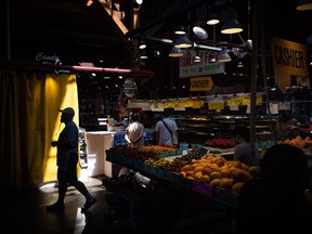 A person is silhouetted as people shop for produce at the Granville Island Market in Vancouver, B.C., Wednesday, July 20, 2022. With food inflation running hot and grocery store profits reaching record highs, the Competition Bureau is looking into whether the sector is contributing to the rising cost of groceries.