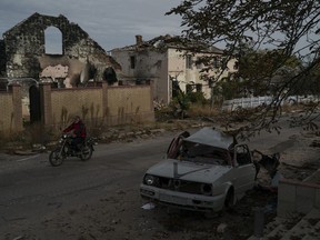 A man drives his motorcycle past a destroyed car in the retaken village of Velyka Oleksandrivka, Ukraine, Wednesday, Oct. 12, 2022.