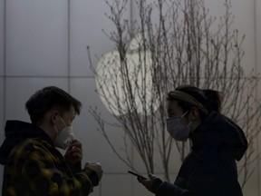 Shoppers stand near the Apple logo in Beijing, China, Wednesday, Feb. 26, 2020. Apple is rolling out a new system that will help iPhone 14 users in Canada reach emergency responders in the event they can't connect to cellular or Wi-Fi service.