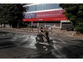A motorcyclist wearing a protective mask rides past a Kotak Mahindra Bank Ltd. branch on a near-empty street in Mumbai, India, on Monday, May 4, 2020. India's central bank Governor Shaktikanta Das and the chief executive officers of the nation's banks have discussed ways to ensure credit flow to businesses once the world's toughest stay-at-home order ends. Photographer: Dhiraj Singh/Bloomberg