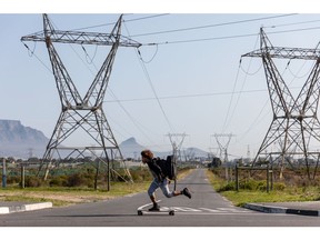 A longboarder skates past electricity transmission towers close to the Eskom Holdings SOC Ltd. Acacia electrical substation in the Monte Vista district of Cape Town, South Africa, on Tuesday, Aug. 2, 2022. South Africa's state-owned power utility Eskom warned it may have to implement rolling blackouts for the first time in more than a week due to a shortage of generation capacity.
