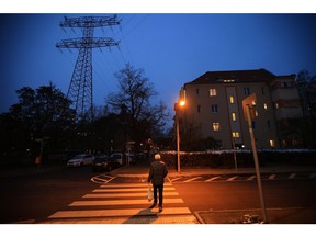 A pedestrian crosses a road near a high voltage electricity transmission tower and partially lit apartment block in a residential district of Berlin, Germany, on Monday, Nov. 21, 2022. The German government plans to collect windfall profits from electricity companies despite legal uncertainties about the proposal, according to a government paper seen by Bloomberg. Photographer: Krisztian Bocsi/Bloomberg