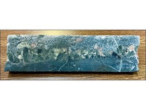 Drill core from 391 m in Hole HK22-018 showing cockade prismatic amphibole (green) and biotite (black) crystals up to 1cm in length growing into a phoscorite vein composed of coarse calcite and apatite (pink). The high core angle large crystal growths suggest a near vertical emplacement and extensional open space. NQ core diameter is 36.5 mm.