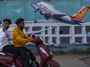 FILE - A scooterist drives past a wall painted with Air India planes in Mumbai, India, Thursday, Jan. 27, 2022. India's oldest and largest conglomerate Tata Sons will merge its Air India with Vistara, which it jointly runs with Singapore Airlines, according to a statement released on Tuesday.
