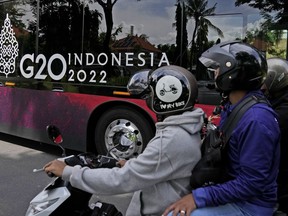 Motorists ride their bikes as a bus with a G20 sticker rolls past in Nusa Dua, Bali, Indonesia, Saturday, Nov. 12, 2022. Indonesia is gearing up to host the gathering of the leaders of the world's biggest economies this coming week.