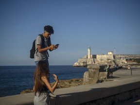 A youth uses his smartphone as he and a friend walk along the Malecon seawall in Havana, Cuba, Friday, Nov. 25, 2022. Ever-widening access to the internet is offering a new opportunity for Cubans looking for hard-to-obtain basic goods: online shopping.