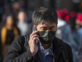 A pedestrian wearing a mask walks down Bay Street at Front Street using a phone in Toronto.