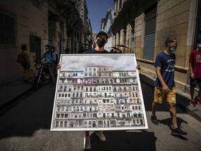 FILE - Photographer Gabriel Guerra Bianchini poses holding his photo collage titled "Hotel Habana 3/10" in Havana, Cuba, March 31, 2021. The photo is the first NFT, Non-Fungible Token, to be auctioned by an artist resident in Cuba, but in 2022, doors began to close for artists like him as key NFT trading platforms have gradually blocked Cuban artists on and off the island from their platforms.