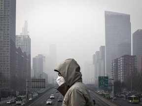A man wearing a face mask walks on a footbridge as buildings shrouded in haze stands in the background in Beijing, China, on Friday, Jan. 6, 2017. Toxic haze that settled over much of China during the last three weeks has triggered a flight reflex among residents, leading to the rising popularity of smog avoidance travel packages to far-flung locations such as Iceland and Antarctica.
