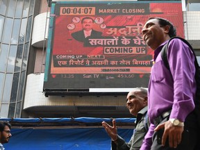 People walk past an electronic board displaying news on the Adani Group at the Bombay Stock Exchange in Mumbai on Jan. 27. Trading in the business empire of Asia's richest man Gautam Adani was halted, following a 15 per cent plunge in its share price, days after the short seller report was released.