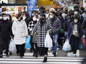 FILE - People with shopping bags walk across a traffic intersection towards a train station near a shopping street in the Ueno district in Tokyo, Friday, Dec. 30, 2022. Japan's consumer inflation rate hit a 41-year high of 4% in December, as prices for everything from burgers to gas surged.
