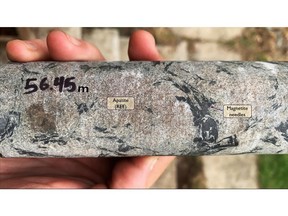 Photograph of drill core from near bedrock surface at the top of drill hole HK20-004, located on the same drill collar as Hole 13, showing altered magnetite needles with reaction rims of pyrite–pyrrhotite–iron carbonate and bastnaesite (LREE)–pyrochlore (Na,Ca)2Nb2O6(OH,F) in a matrix of apatite with calcite inclusions containing monazite ((Ce,La,Nd,Th)PO4), quartz and potassium feldspar. The magnetite-quartz-potassium feldspar assemblage is a high temperature potassic alteration facies.