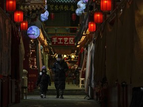 A man and a child wearing face masks walk by shuttered stores on Jan. 3, 2023, which would be selling souvenirs in Qianmen, a popular tourist spot in Beijing. China's business and consumer activity might revive as early as the first quarter of this year, but before that happens, entrepreneurs and families face a painful squeeze from a surge in cases that has left employers without enough healthy workers and kept wary customers away from shopping malls, restaurants, hair salons and gyms.
