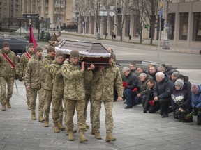 People kneel as the Ukrainian servicemen carry the coffin of their comrade Oleh Yurchenko killed in a battlefield with Russian forces in the Donetsk region during a commemoration ceremony in Independence Square in Kyiv, Ukraine, Sunday, Jan. 8, 2023.
