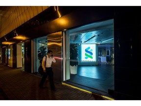 A pedestrian walks past signage illuminated inside a Standard Chartered Plc bank branch at night in Hong Kong, China, on Thursday, July 25, 2019. Standard Chartered is scheduled to release interim earnings results on Aug. 1. Photographer: Paul Yeung/Bloomberg