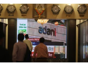 People walk past a screen displaying news featuring on Adani Group inside the BSE building in Mumbai, India, on Thursday, Feb. 2, 2023. Adani's businesses have lost $107 billion in a week, one of the biggest wipeouts in India's history, after an explosive report by short-seller Hindenburg Research forced him to pull a stock sale at the 11th hour and led some lenders to reject his securities as collateral for client trades. Photographer: Dhiraj Singh/Bloomberg