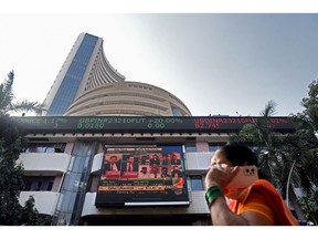 A pedestrian passes a news broadcast on the Adani Group outside the Bombay Stock Exchange (BSE) building in Mumbai, India, on Thursday, Feb. 9, 2023. Adani stocks fell, ending a two-day rally, after MSCI Inc. said it was reviewing the amount of shares linked to the group that were freely tradable in public markets.