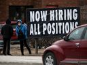 A person standing near a sign indicating a local business is hiring.
