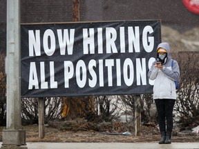 A person standing beside a large sign indicating that a business is hiring all positions in Winnipeg.