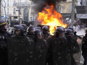 Riot police officers stand by a burning car during clashes at a demonstration against plans to push back France's retirement age, in Paris, Saturday, Feb. 11, 2023. France is bracing itself for a fourth round of nationwide protests against President Emmanuel Macron's plans to reform pensions but key transports unions have not called for strikes allowing trains and the Paris metro to run this time.